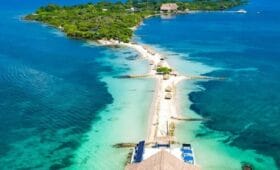 Vista aérea de Isla Palma, una isla tropical cerca de Cartagena, con aguas turquesas, exuberante vegetación, una playa de arena y una estructura con techo de paja que se extiende hacia el mar, perfecta para una escapada idílica de 3 días.