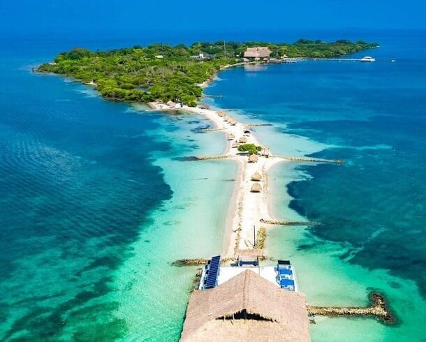 Vista aérea de Isla Palma, una isla tropical cerca de Cartagena, con aguas turquesas, exuberante vegetación, una playa de arena y una estructura con techo de paja que se extiende hacia el mar, perfecta para una escapada idílica de 3 días.