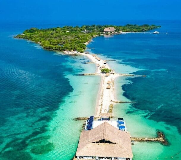 Vista aérea de Isla Palma, una isla tropical cerca de Cartagena, con aguas turquesas, exuberante vegetación, una playa de arena y una estructura con techo de paja que se extiende hacia el mar, perfecta para una escapada idílica de 3 días.