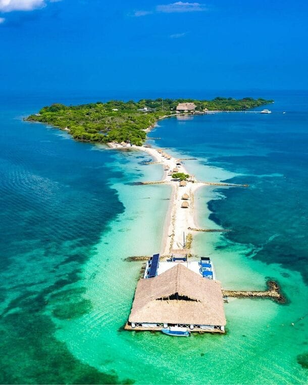 Vista aérea de Isla Palma, una isla tropical cerca de Cartagena, con aguas turquesas, exuberante vegetación, una playa de arena y una estructura con techo de paja que se extiende hacia el mar, perfecta para una escapada idílica de 3 días.