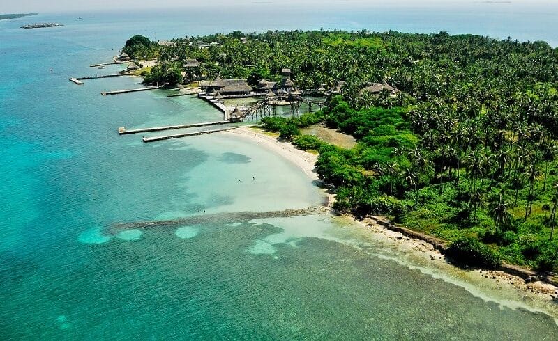 La vista aérea de Isla Múcura cerca de Cartagena revela aguas cristalinas de color turquesa, playas de arena, exuberante vegetación y edificios esparcidos entre densas palmeras en esta serena porción terrestre.