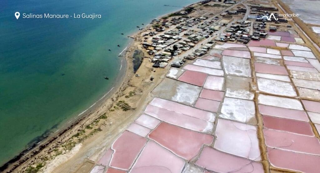 Vista aérea de Salinas Manaure en La Guajira, Colombia, que muestra salinas rosadas cerca de la costa y un pequeño asentamiento costero en la Alta Guajira.