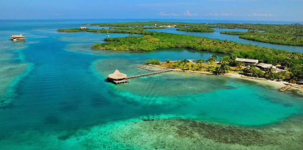 Vista aérea de Isla Tintipán, una isla tropical cerca de Cartagena, con aguas turquesas, exuberante vegetación verde y pequeñas cabañas sobre muelles que se extienden hacia el agua. Perfecto para una escapada serena de 4 días.