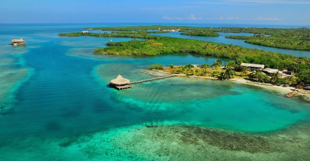 Vista aérea de Isla Tintipán, una isla tropical cerca de Cartagena, con aguas turquesas, exuberante vegetación verde y pequeñas cabañas sobre muelles que se extienden hacia el agua. Perfecto para una escapada serena de 4 días.